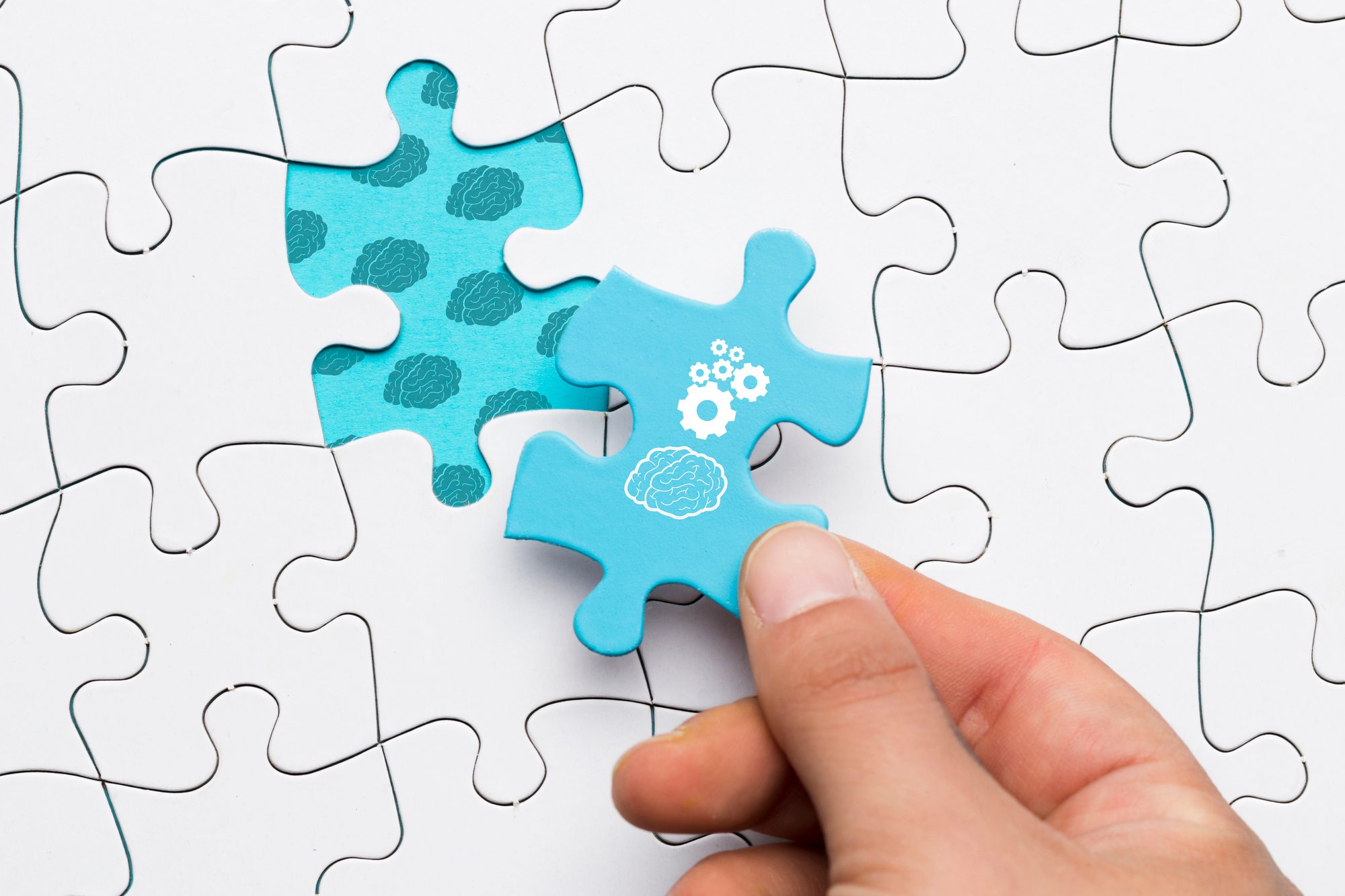 close-up-human-hand-holding-blue-puzzle-piece-with-brain-cogwheel-drawing